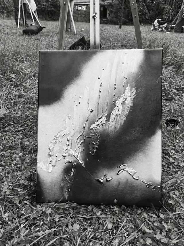 An abstract black-and-white painting in the grass, in front of an easel