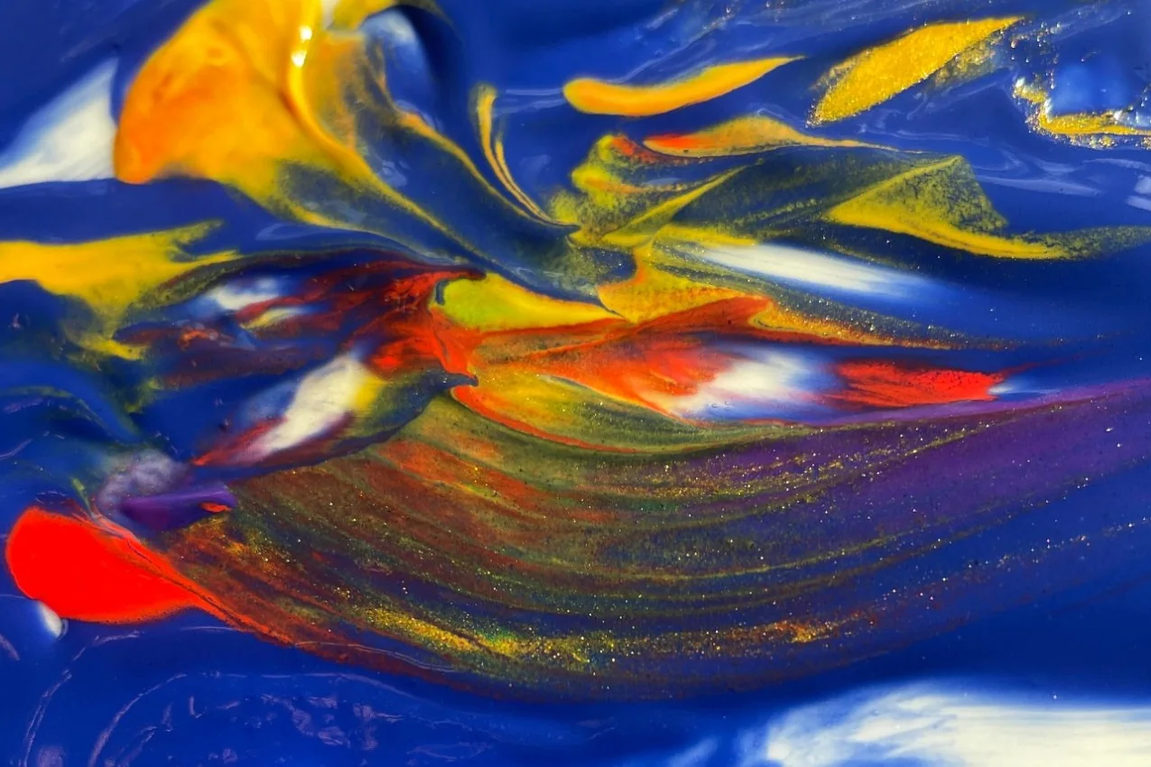Close-up of wet paint: yellow, orange and red swirling through deep blue